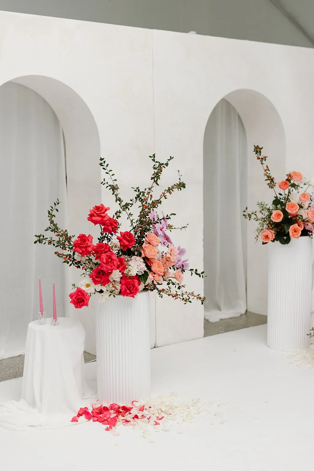 Large statement floral arrangement with peach roses, pink blooms, and greenery displayed in a tall white plinth.