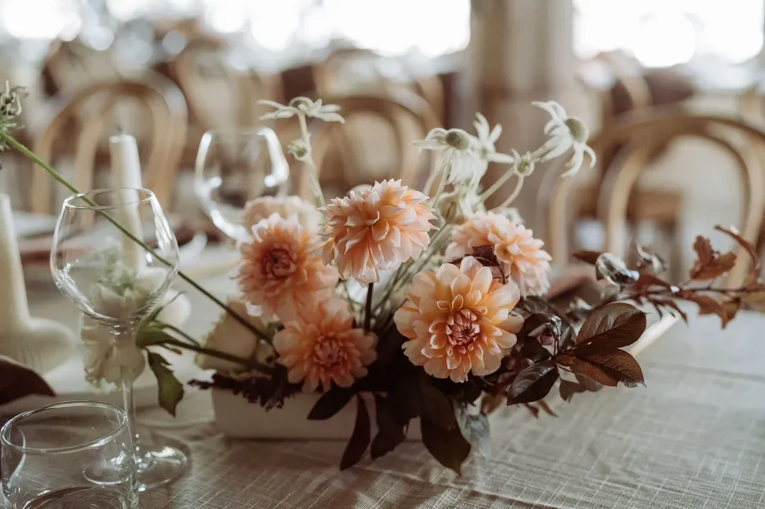 Peach-toned dahlias and delicate foliage arranged in a low modern vase on the wedding reception table.