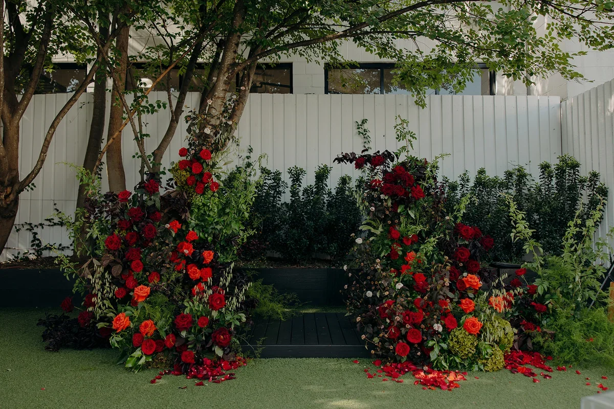 Wide view of lush red rose pillars framing the ceremony aisle in a garden setting.