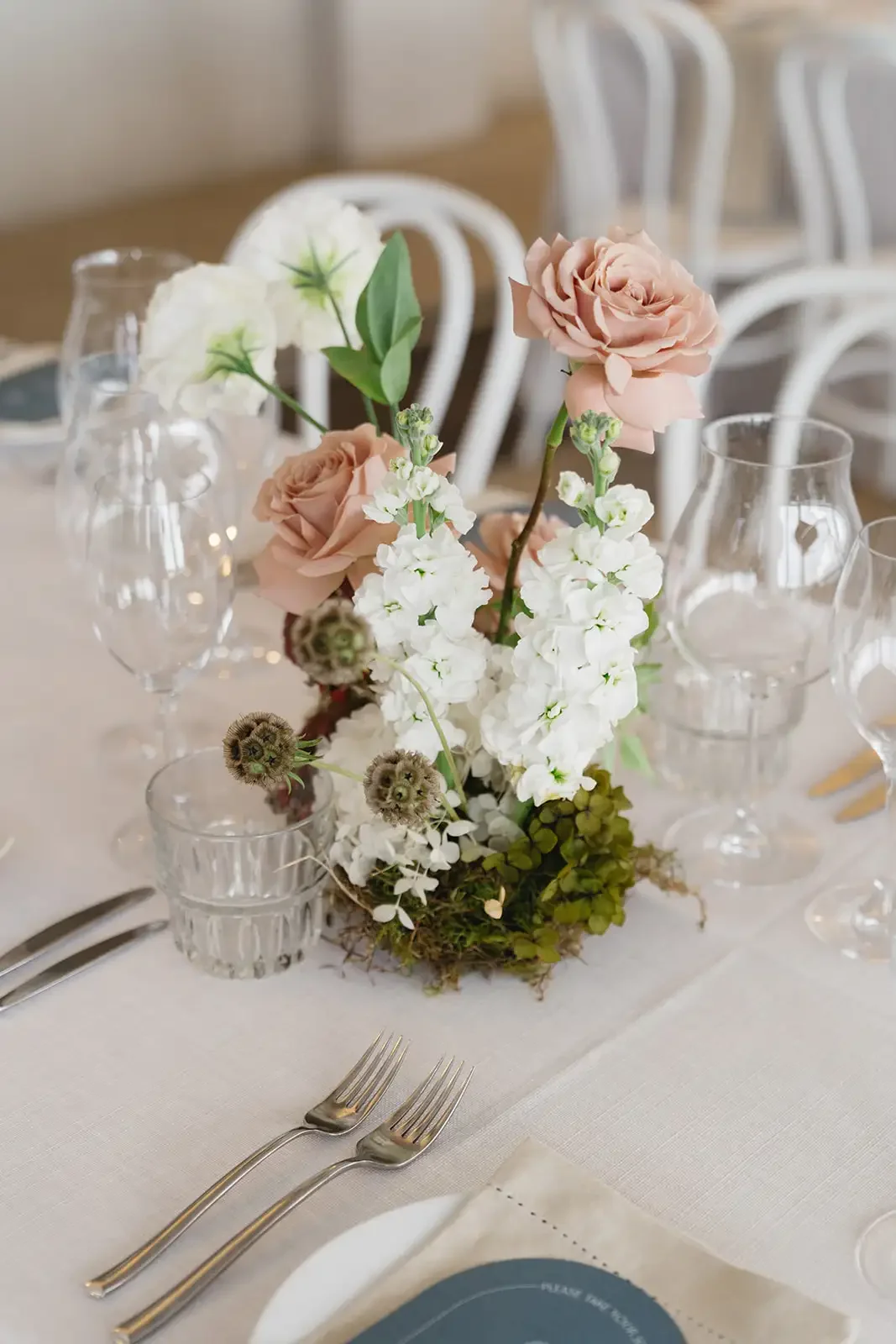 Wedding reception table decor with white and blush florals, moss and minimalist place settings.