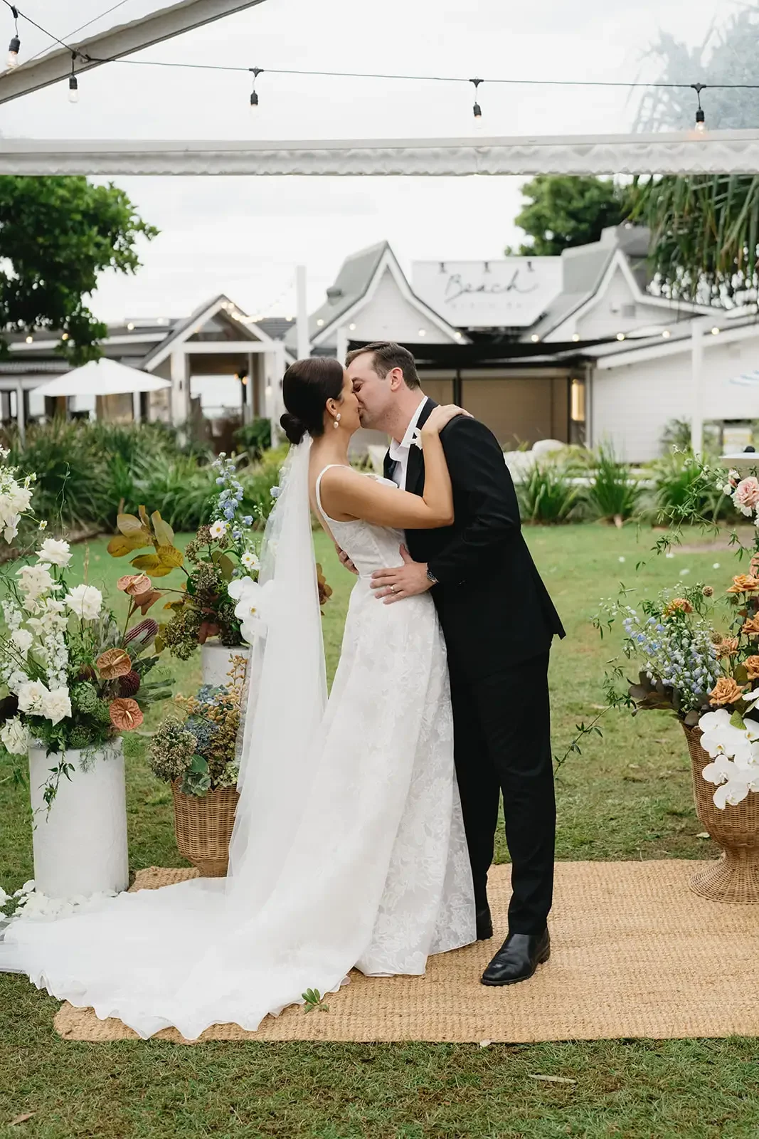 Bride and groom sharing their first kiss surrounded by natural floral arrangements in Byron Bay.