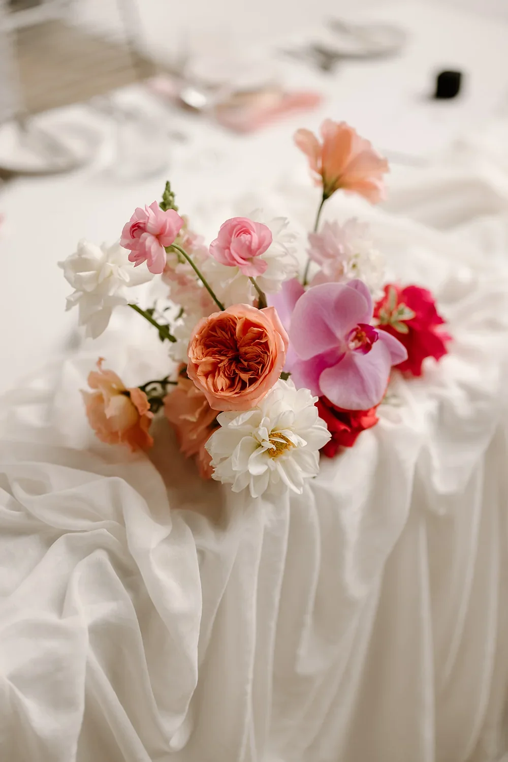 Close-up of a pastel wedding table arrangement featuring peach roses, pink dahlias, and white blooms on soft draped linen.