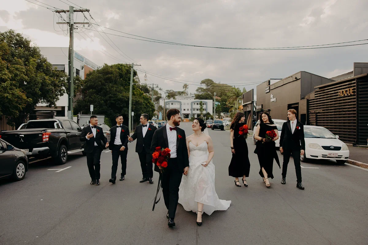 Bridal party walking together down a Brisbane street holding red wedding bouquets.