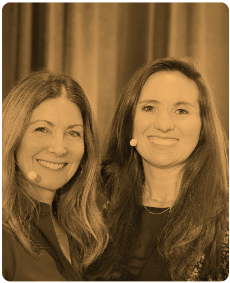 Two women smiling, wearing lapel microphones, in a sepia-toned photograph with a curtain backdrop.