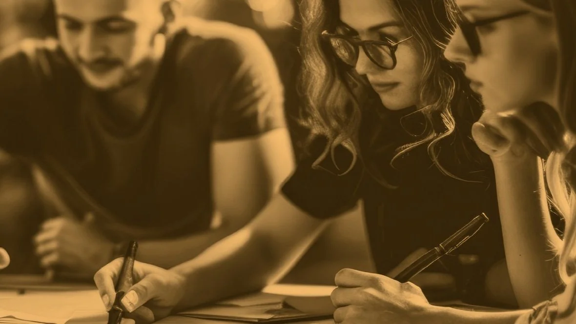 Three people collaborating, writing on paper, wearing glasses, sepia filter.