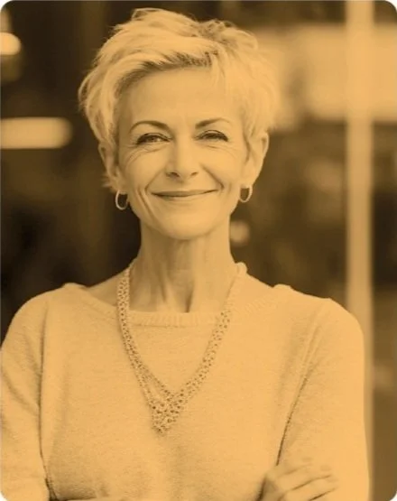 A grayscale image of a woman with short hair wearing a sweater and a necklace, smiling at the camera.