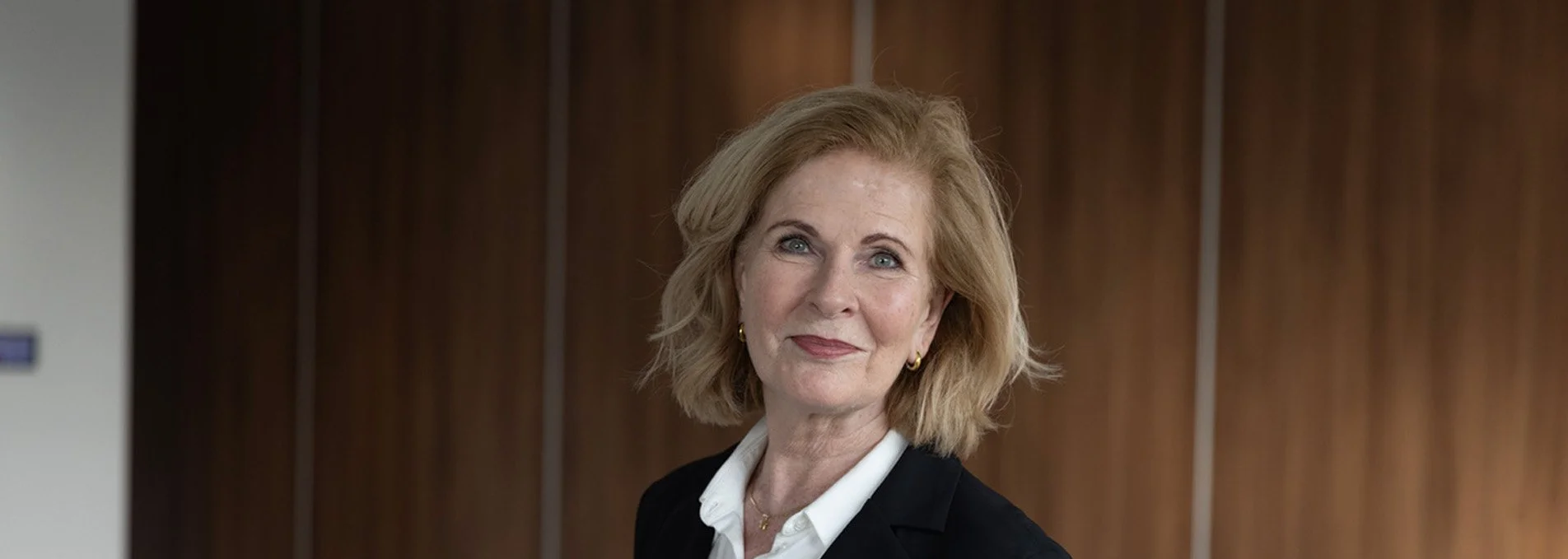 Een elegante, seniore vrouw met kort blond haar en mantelpak.
