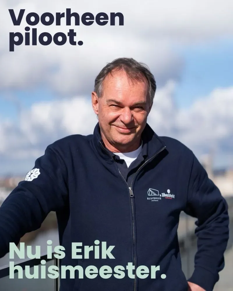 Erik, huismeester bij Sluishuis in Amsterdam, draagt een Sluishuis × ZilverWerkt-jack tegen de Amsterdamse skyline.