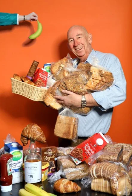 Edwin Maas (72), ZilverWerker en Kiwi van de Maand bij Redkiwi, lacht met armen vol broden en lunchproducten