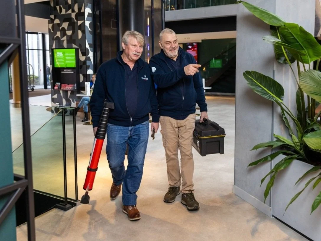 Twee seniore mannen lopen met gereedschap door een hotel.