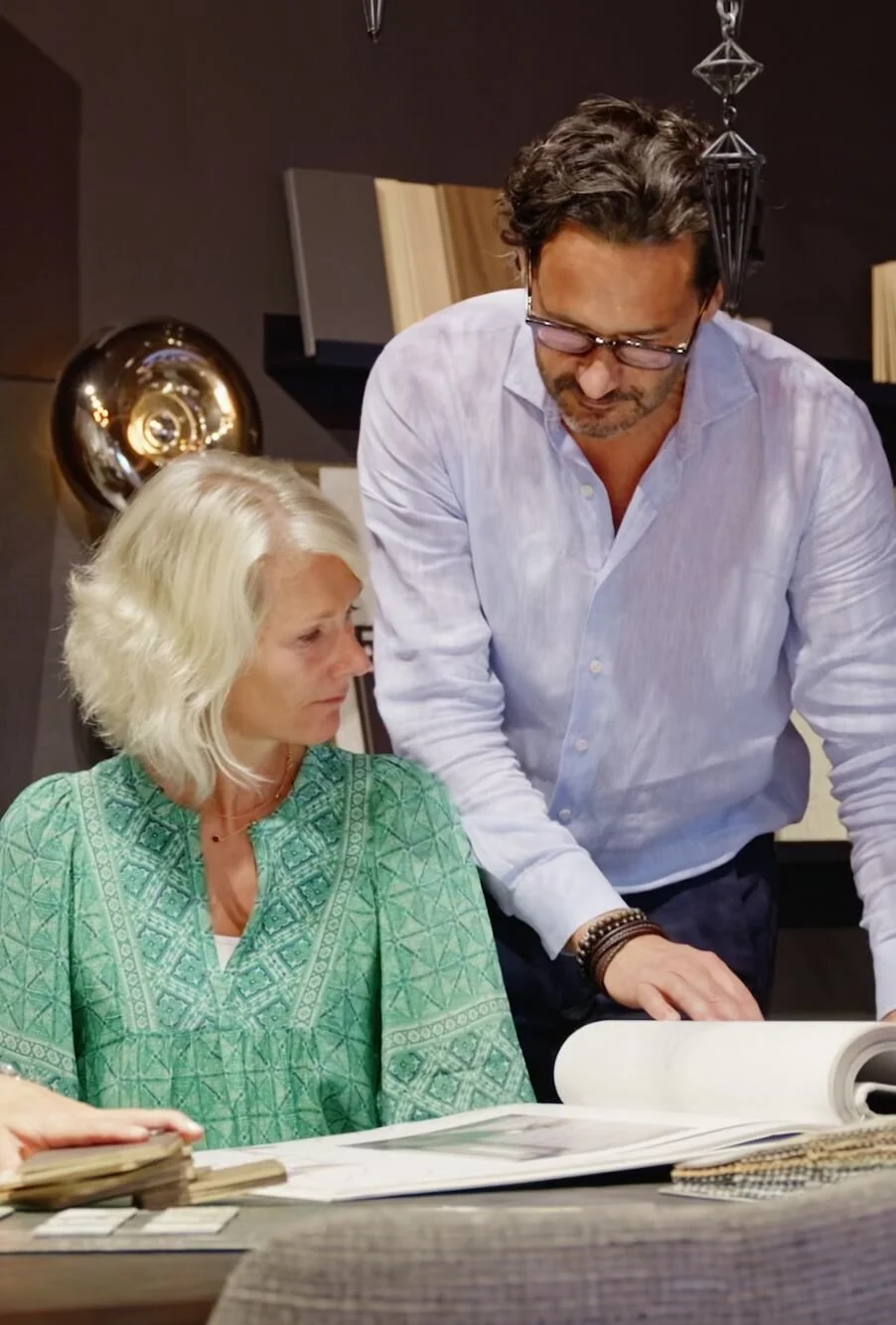 Un homme et une femme discutent devant des documents ou des plans, dans un environnement intérieur moderne.