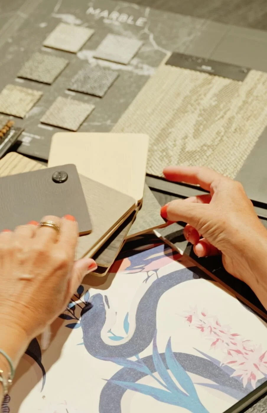 Une personne feuillette un nuancier de couleurs avec des échantillons de matériaux d'intérieur, entourée de plans et d'échantillons de revêtements de sol.