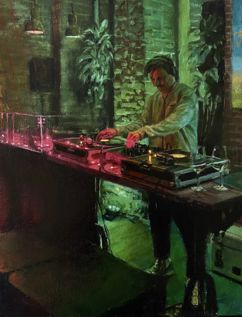 A man wearing glasses, a jacket, and gloves is DJing with turntables in a dimly lit room with green lighting, brick walls, and plants.