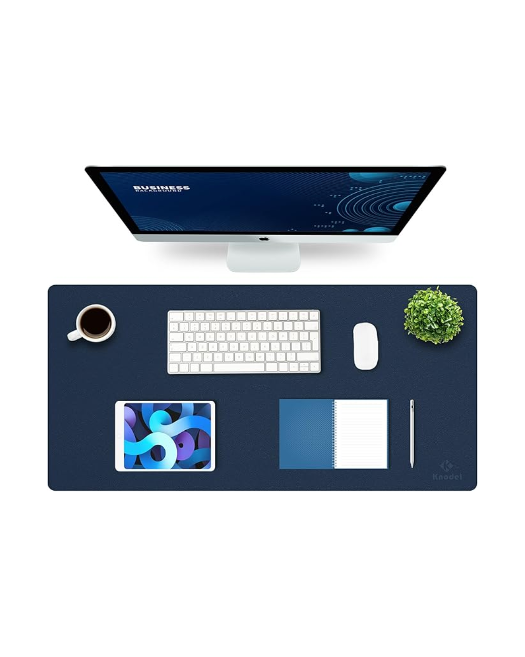 Overhead view of a workspace with a desktop computer, keyboard, mouse, coffee mug, tablet, notebook, pen, and a green potted plant on a dark blue desk mat.