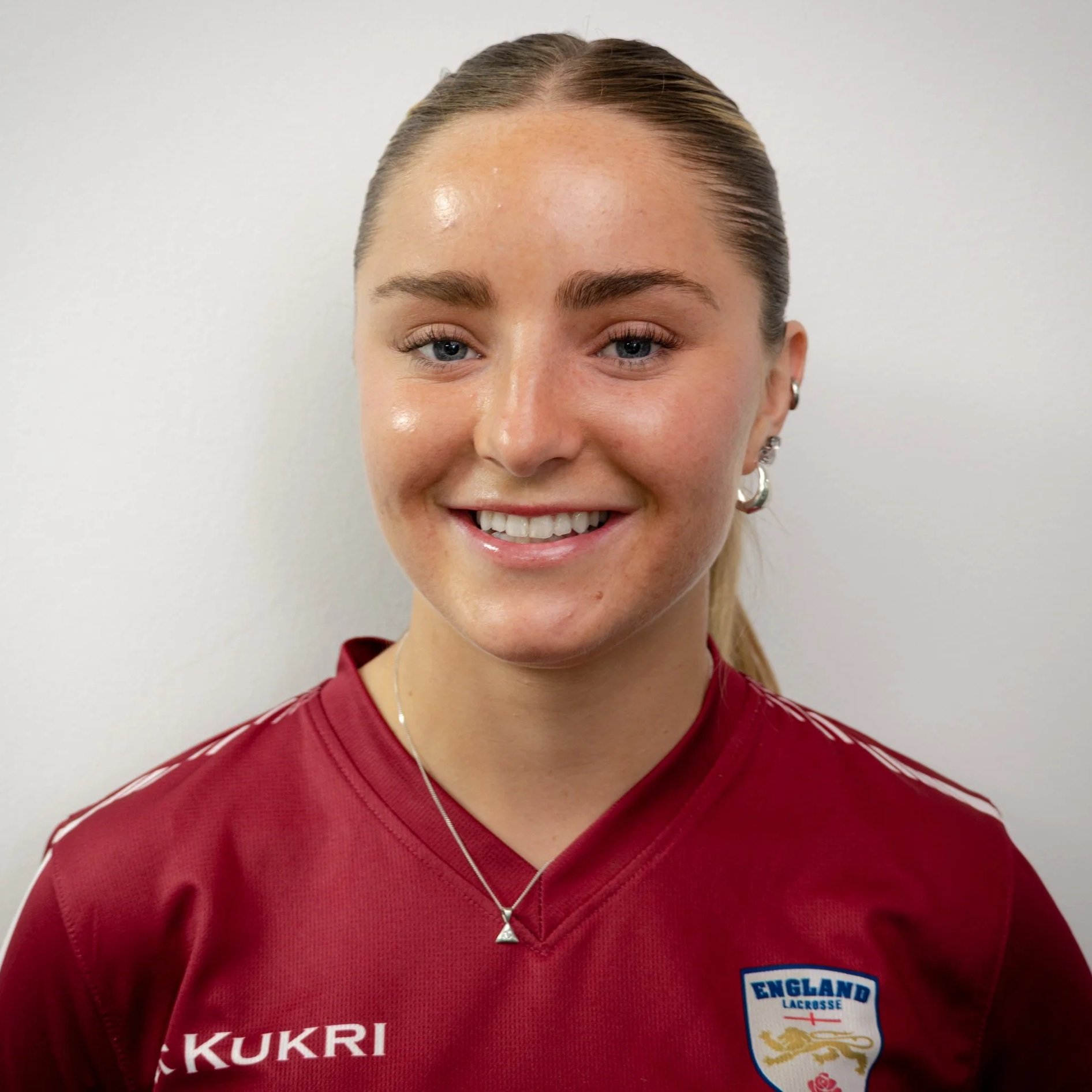 Person wearing a red England Lacrosse jersey with 'World Championships 2022' text, smiling.