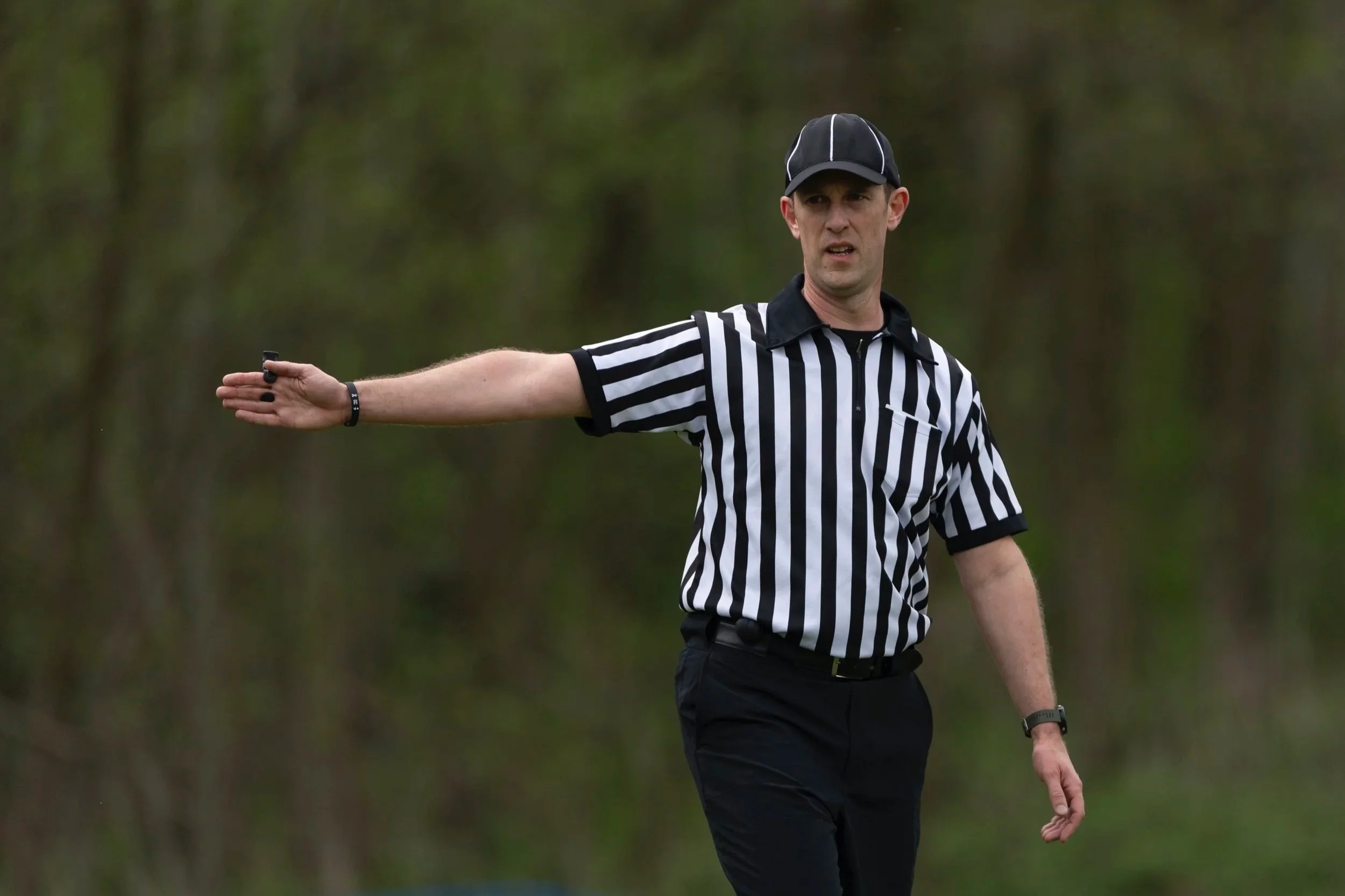 Official with right arm outstretched and whistle in hand