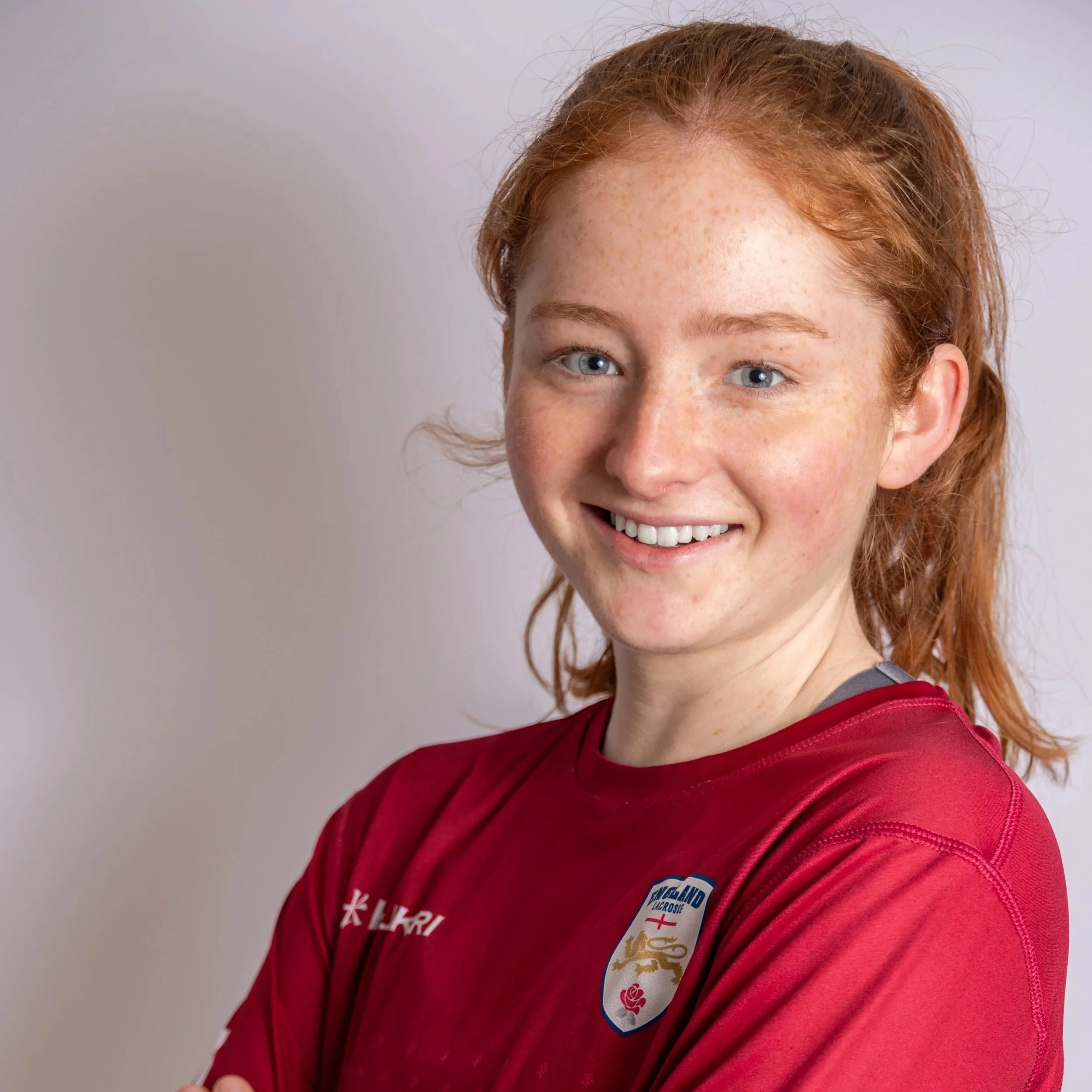 A young person with red hair is smiling and wearing a red long-sleeve shirt with "World Championships 2022" text on the arm and an emblem on the chest.