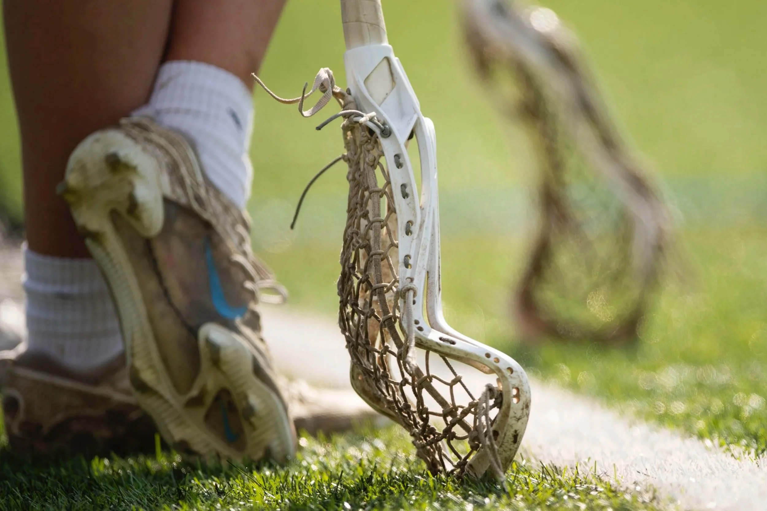 Close up image of lacrosse stick with players feet behind