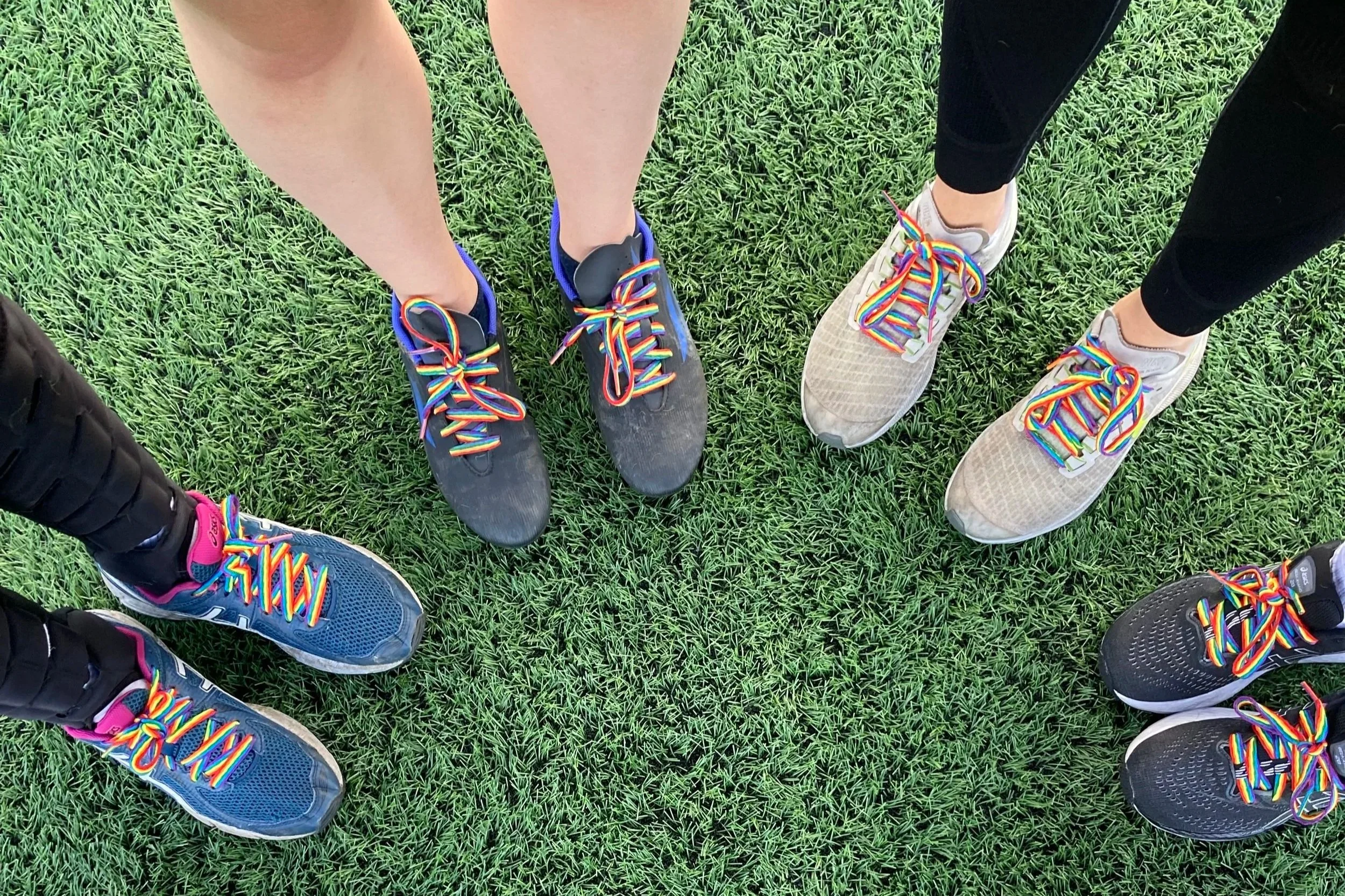 Four people's shoes with rainbow laces in a semi-circle