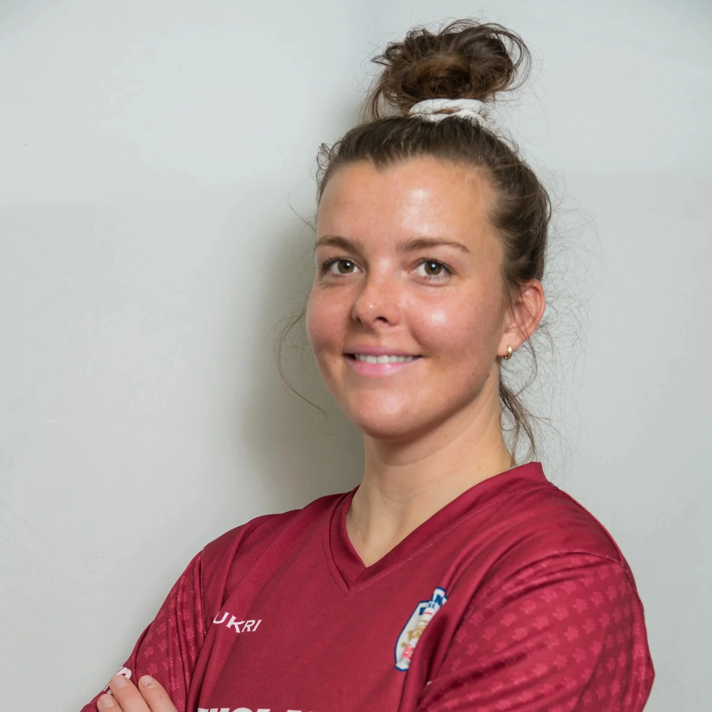 Person wearing a maroon England sports jersey, smiling with arms crossed.