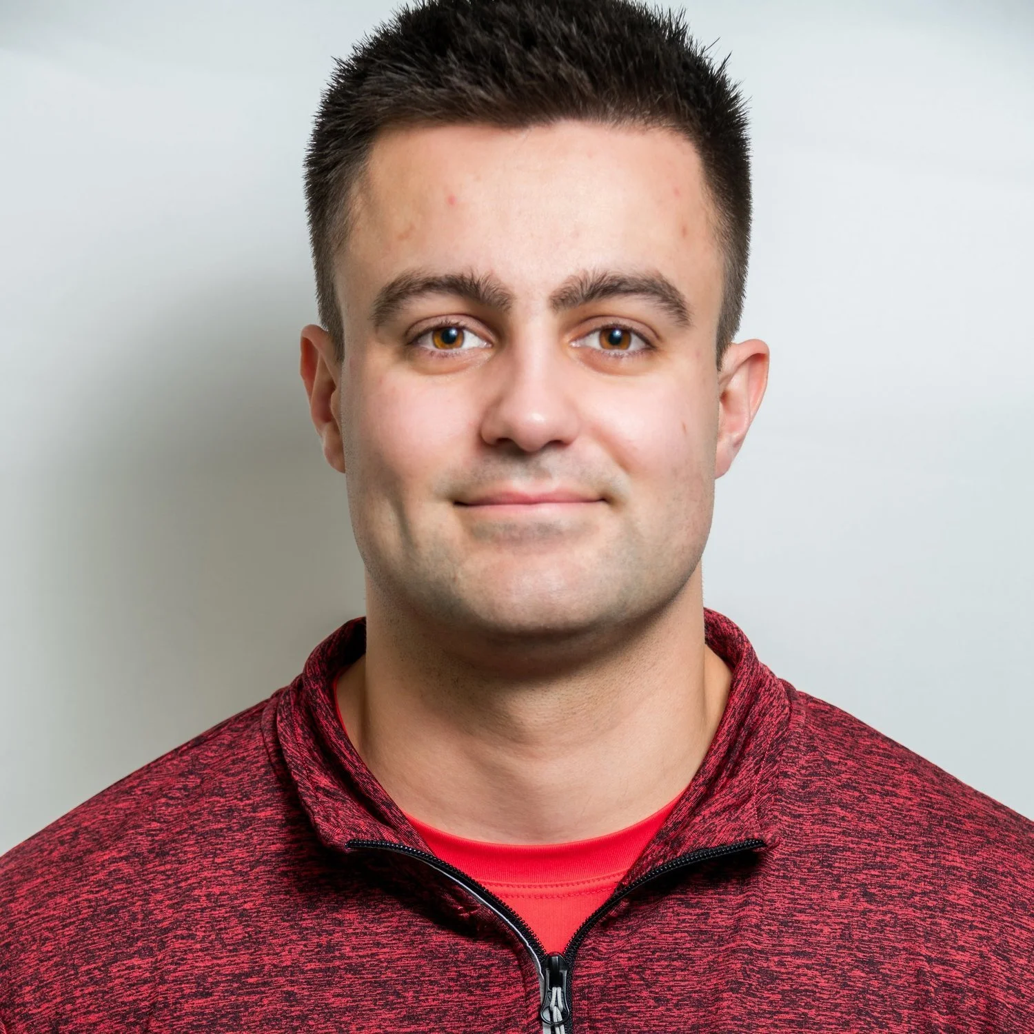 Person wearing a red zip-up jacket against a plain background.