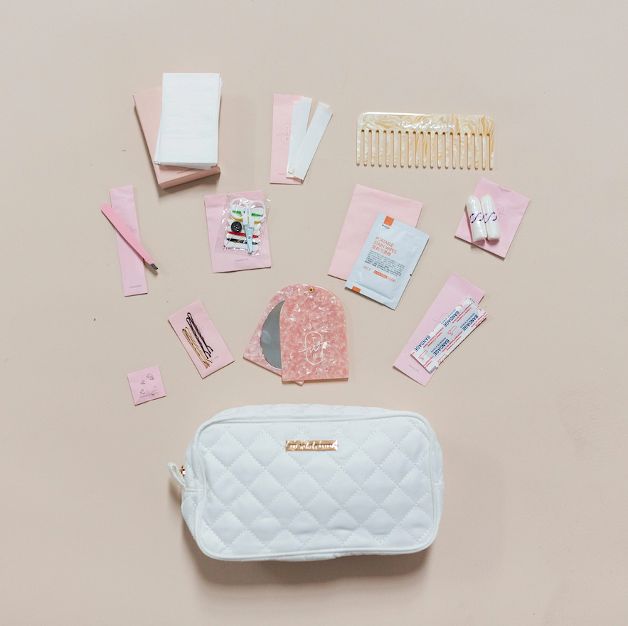 A white quilted cosmetic bag surrounded by various pink and white beauty and personal care items, including cotton pads, hair clips, a comb, bandages, and small packages, all arranged on a light beige background.
