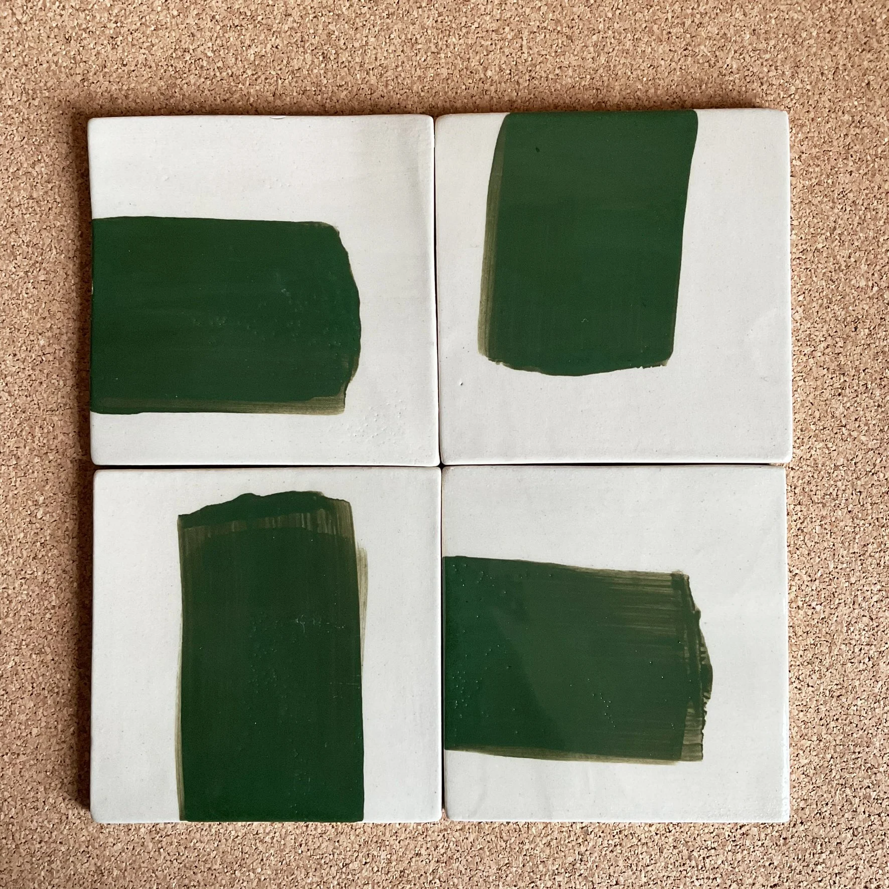 Quatre carreaux en céramique avec des motifs verts sur fond blanc, disposés en carré sur une surface en bois.