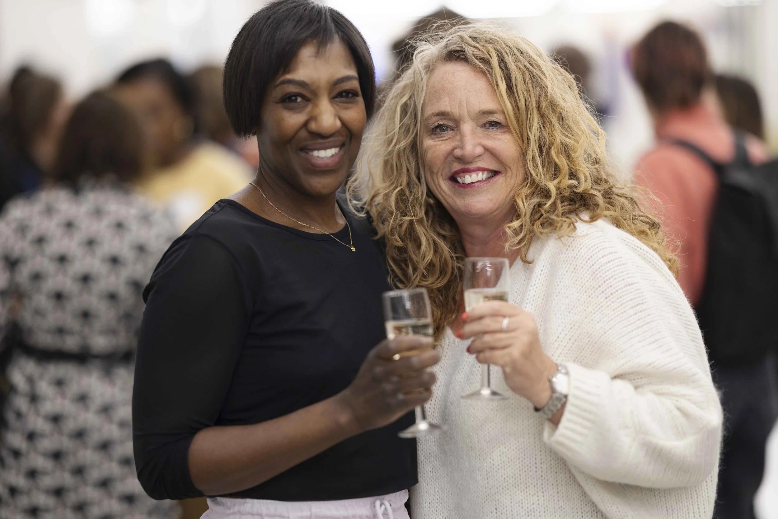 Two women smiling and holding glasses of champagne at a social event