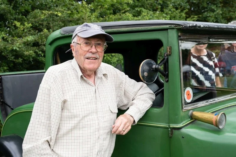 An older gentleman stands proudly beside his 1930s car