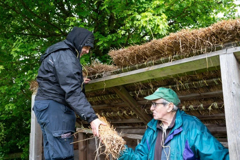 Two people thatching a roof using straw