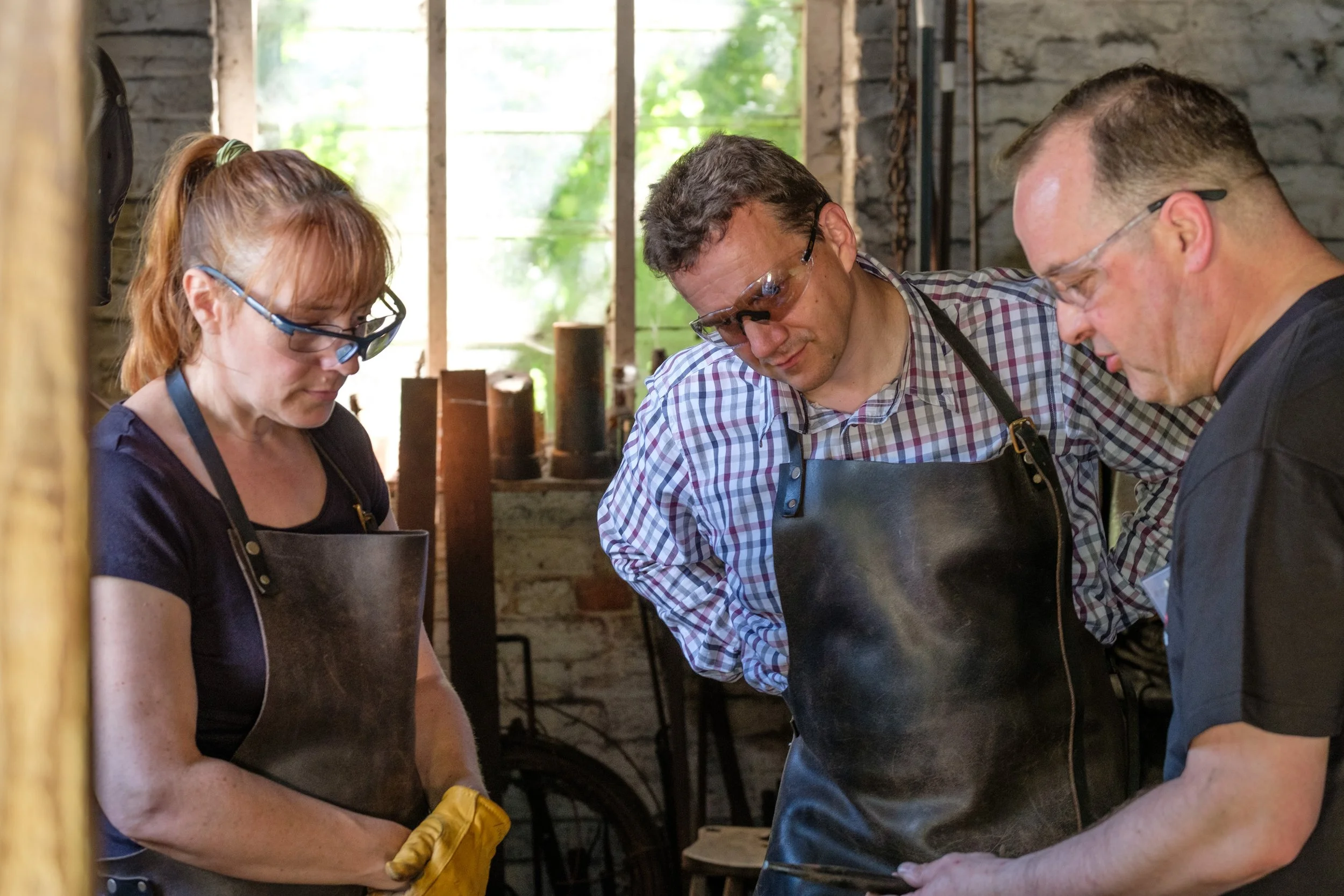 A blacksmith teaching a man and woman to bend metal in a Victorian blacksmiths forge at Chiltern Open Air Museum