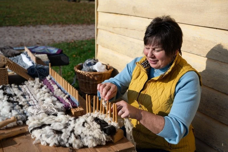 A woman weaves wool on a peg loom