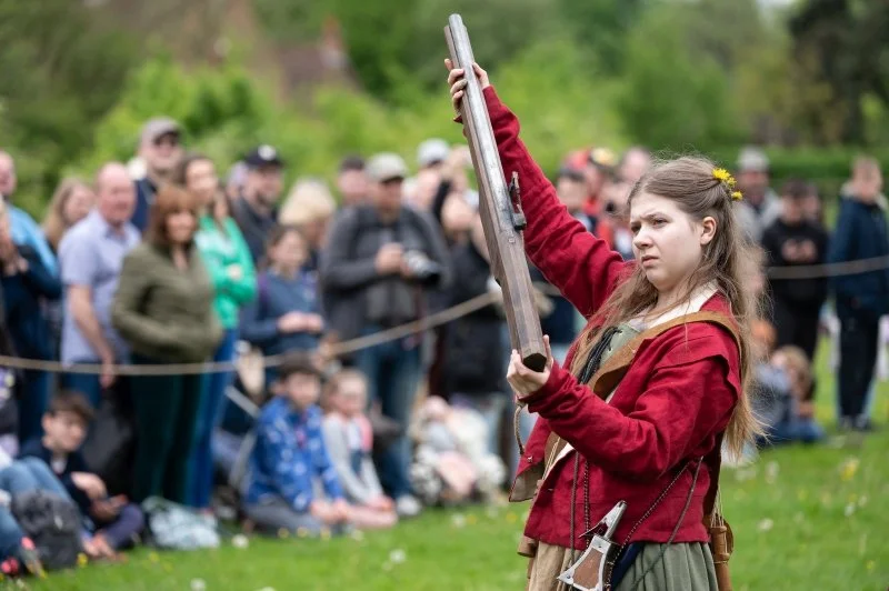 A teenage girl dressed as an Elizabethan soldier holds up a replica gun
