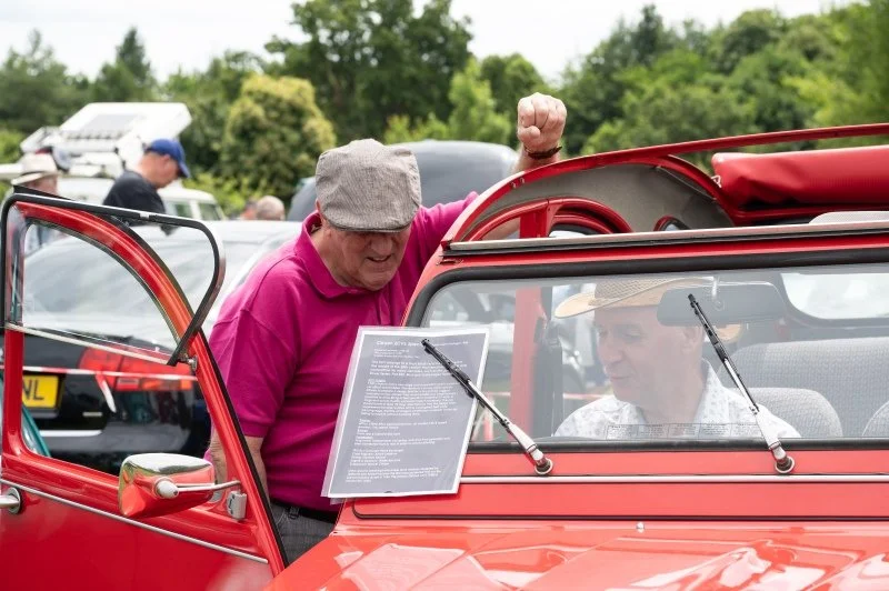 A man in a flat cap talking to a man in a vintage car