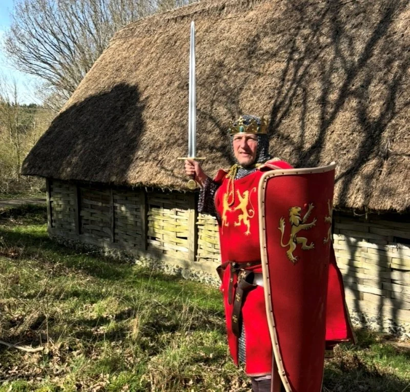 A re-enactor dressed as Richard the Lionheart brandishes a sword outside a barn at Chiltern Open Air Museum