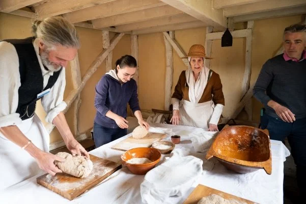 Visitors to the museum help two costumed re-enactors make bread in an 18th century cottage