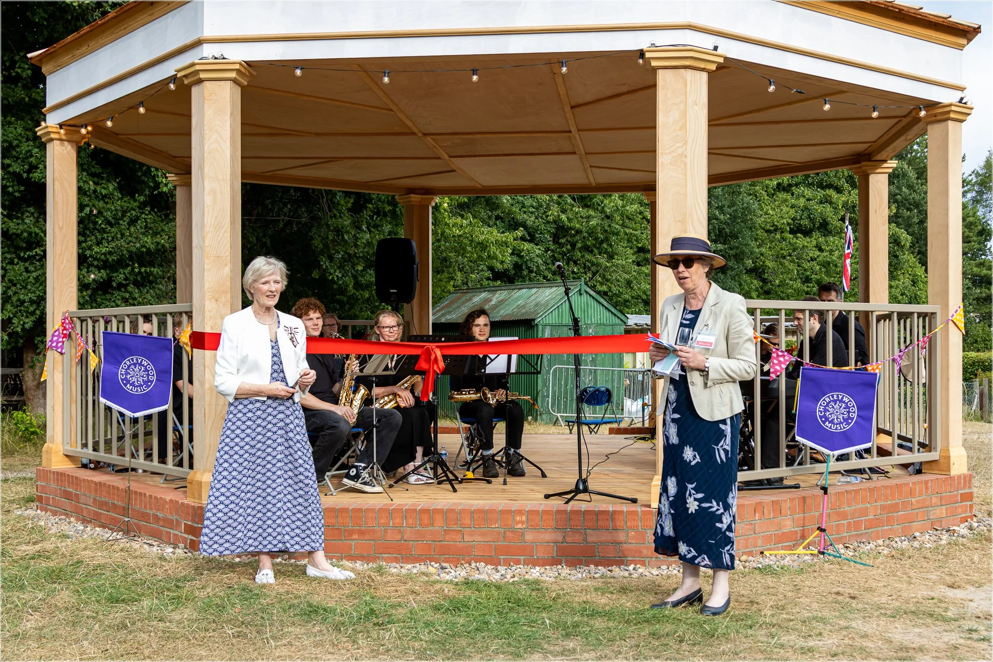 Two ladies stand in front of a red ribbon on a wooden bandstand