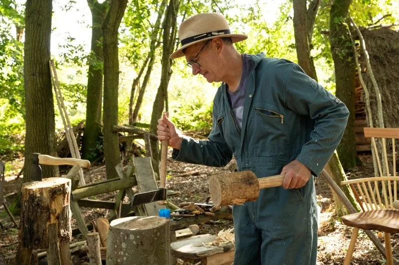 A man stands in a Bodgers camp in the woods surrounded by chair making tools