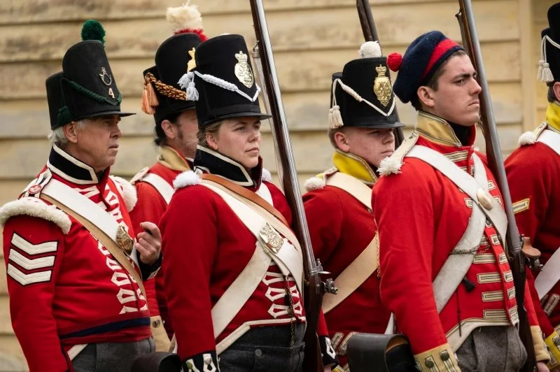 Re-enactors dressed as Napoleonic soldiers with red uniforms line up to perform a drill