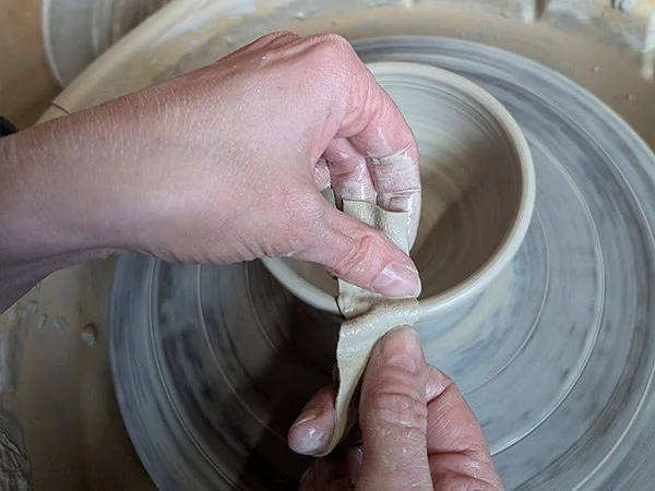 Hands working clay on a pottery wheel
