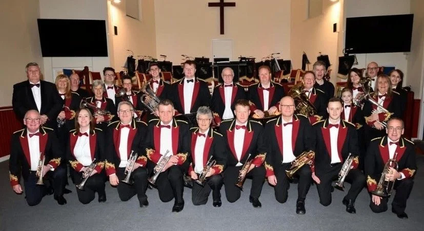 A group photo of a large brass band in smart red and black outfitsholding their instruments