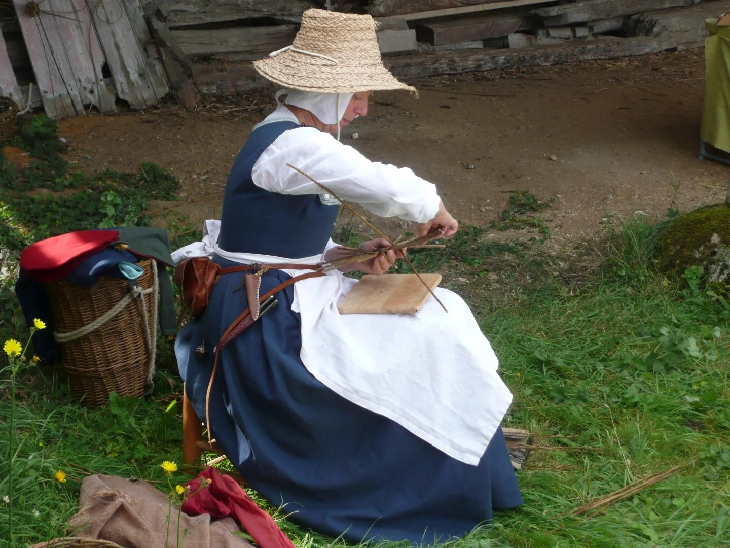 A lady dressed like a Tudor rural worker is weaving a basket from twigs
