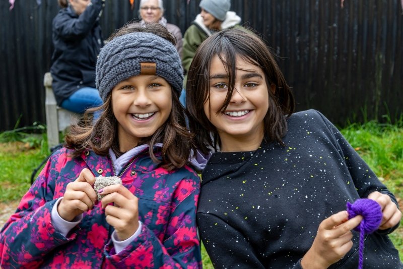Two teenage girls smiling and showing their knitted creations