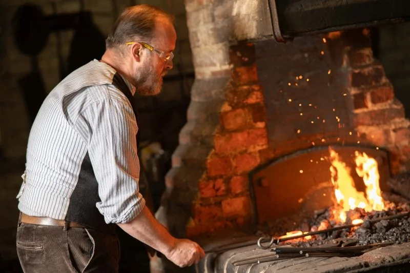 A blacksmith attending the fire in a traditional Victorian forge at Chiltern Open Air Museum