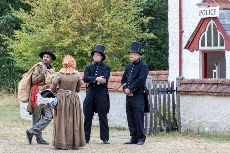 two victorian police officers talking to a man and women dressed in ragged Victorian clothing