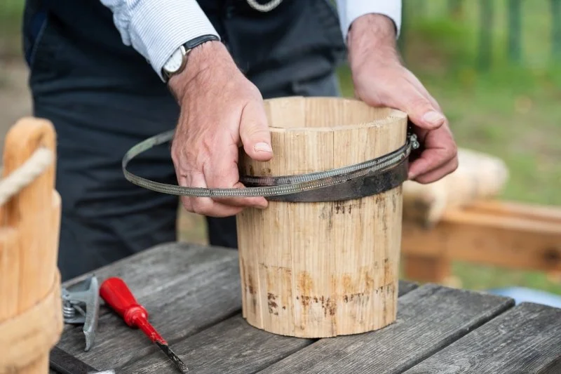 A close up of  a man's hands holding together the wooden pieces that make a traditional bucket