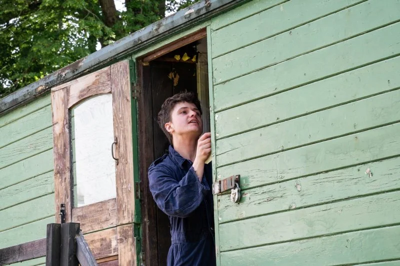 A person painting the doorway of a wooden caravan.