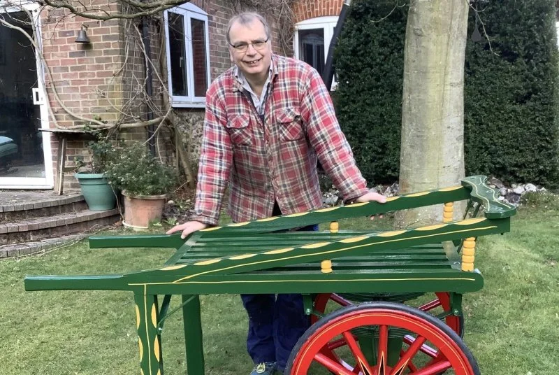 A smiling man stands behind a hand painted wooden cart