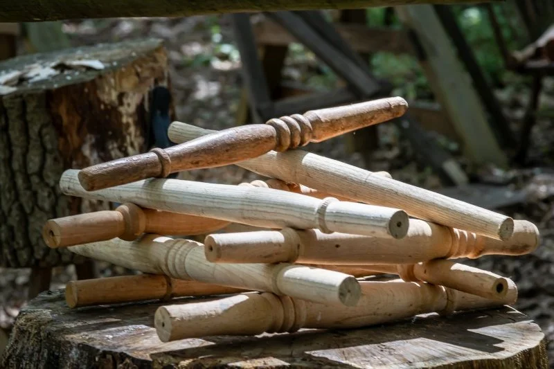 A carefully stacked pile of wooden chair legs sits on a tree stump in the woods