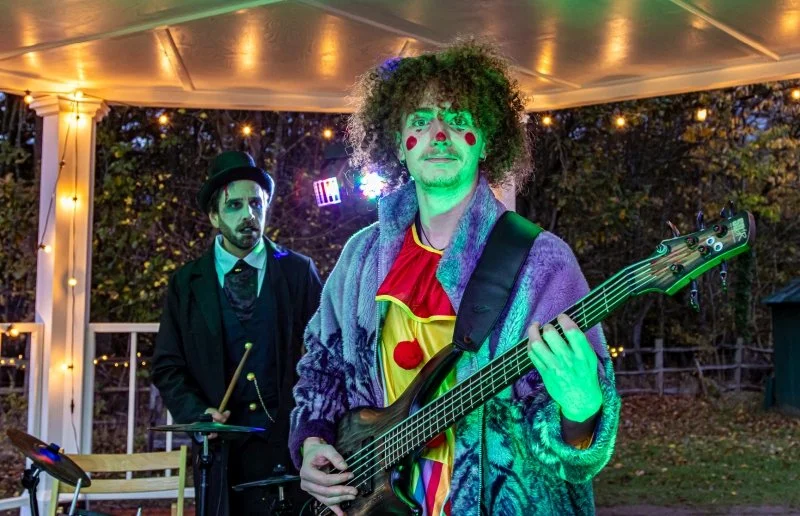 Two men dressed in Halloween costumes are playing instruments on a 1950s bandstand